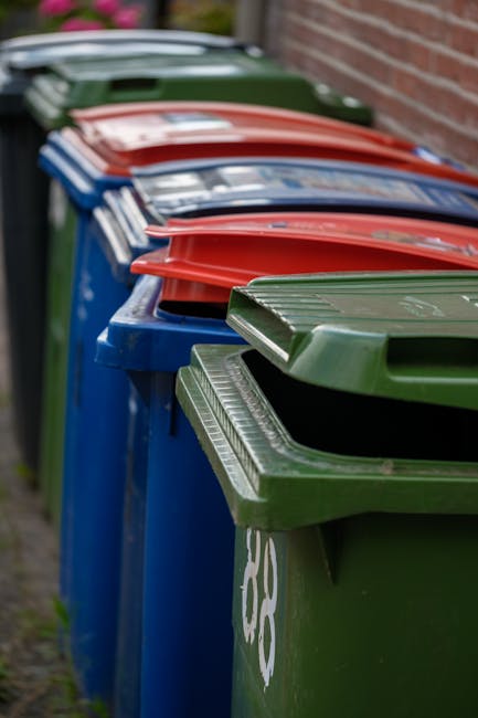 A pile of discarded cardboard boxes, including some flattened and others partially intact, stacked against a rough brick wall and a concrete block wall in an outdoor setting. The boxes vary in size an